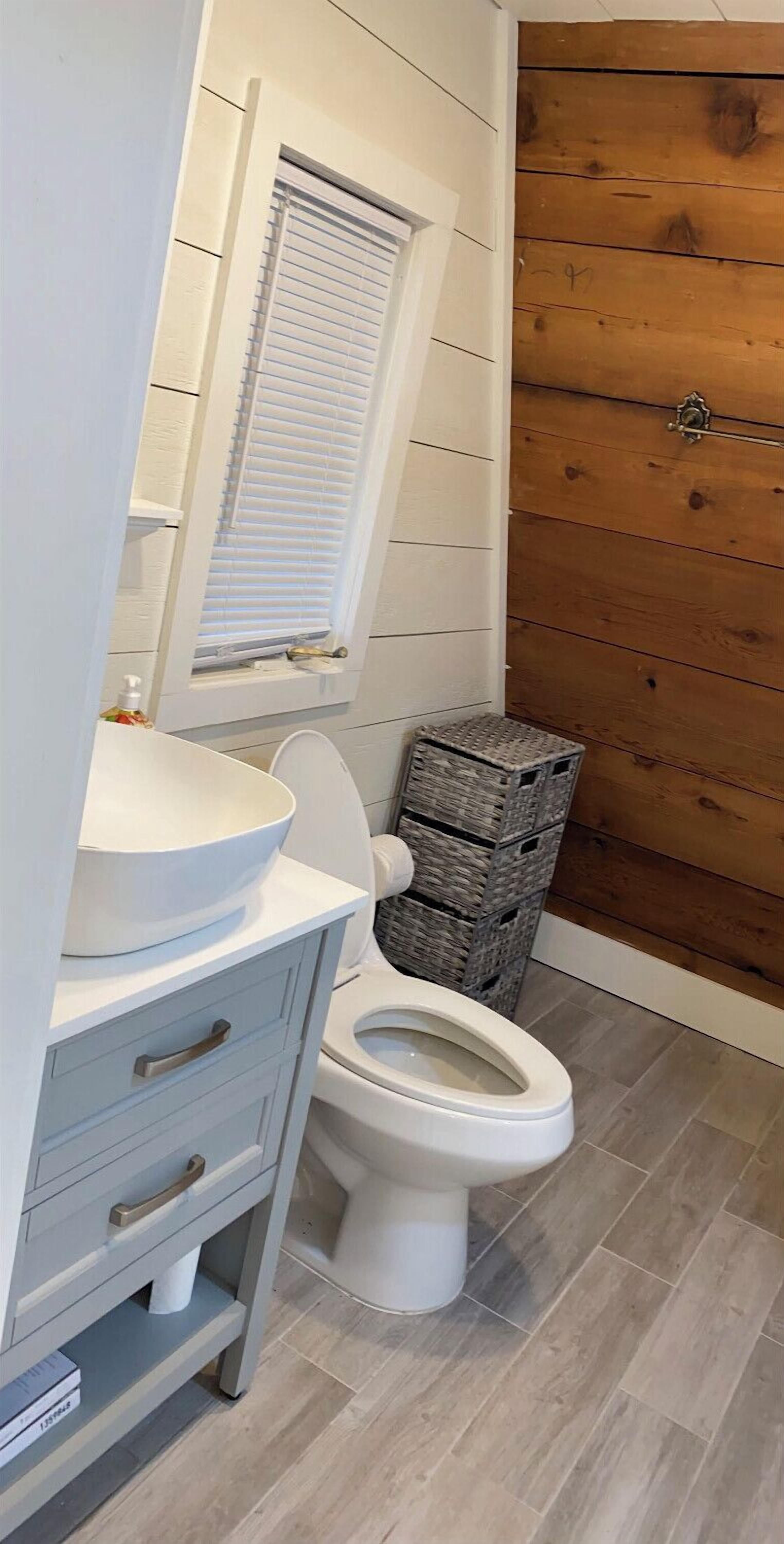 Un bagno con un mobile lavabo bianco, un water e una parete in legno.