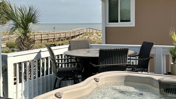 Un balcon avec un jacuzzi, des meubles en osier et une vue sur la plage.
