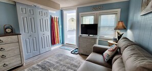 A living room with a beige sofa, a television, a dresser, and a door leading to a balcony.