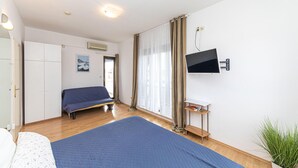 Un dormitorio con cama, armario, televisión en la pared y ventana con cortinas.