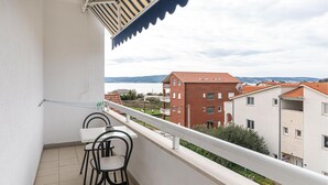 Un balcón con mesa y sillas, con vistas a una zona residencial con edificios de techo rojo y una masa de agua al fondo.