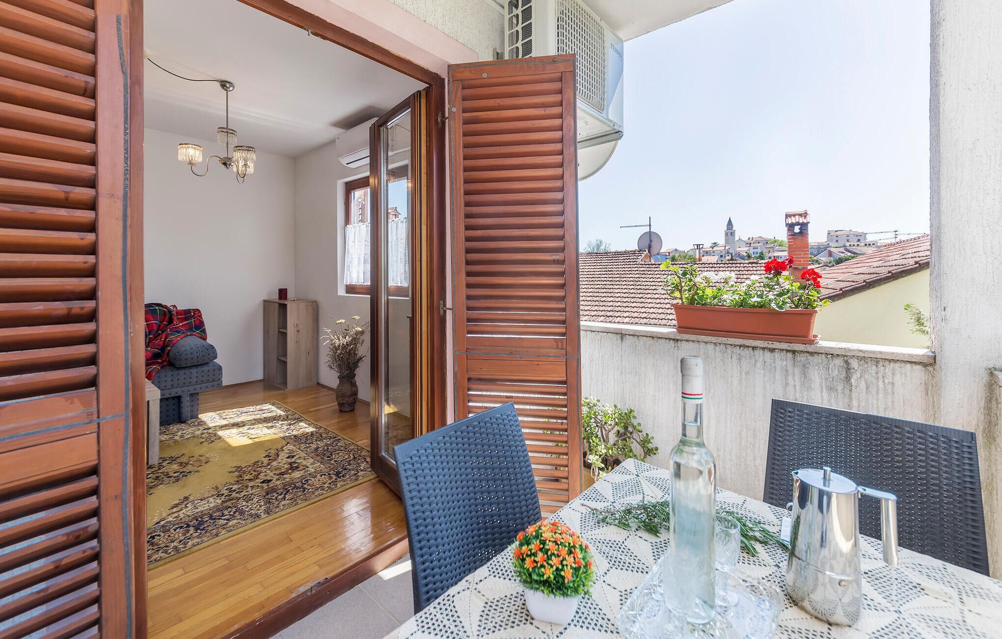 A balcony with a table set for dining, a chair, a potted plant, and a view of the cityscape.