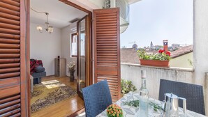 Een balkon met een eettafel, een stoel, een bloempot en uitzicht op de stad.