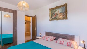 Een slaapkamer met een bed, nachtkastje, lamp, spiegel en een deur naar een badkamer.