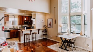 A spacious kitchen with wooden cabinets, a dining area with a table and chairs, and a large window with a view of trees. - Boardwalk Loft w/bay view loacated in old town (Eureka)