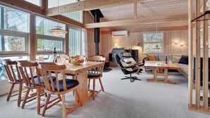 Acogedor interior de cabaña con comedor, chimenea y zona de estar con sofá y sillones.