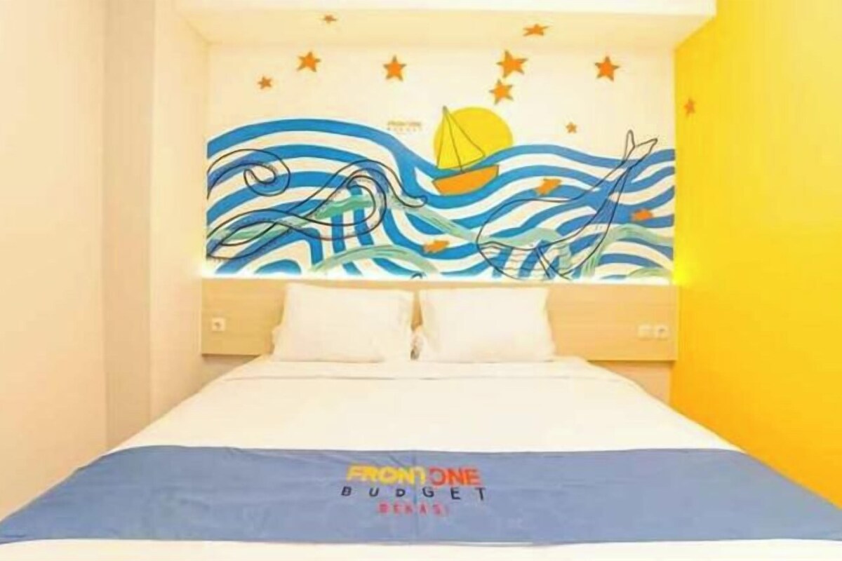 A bed with a blue bedspread, a headboard with a nautical mural, and a yellow accent wall.