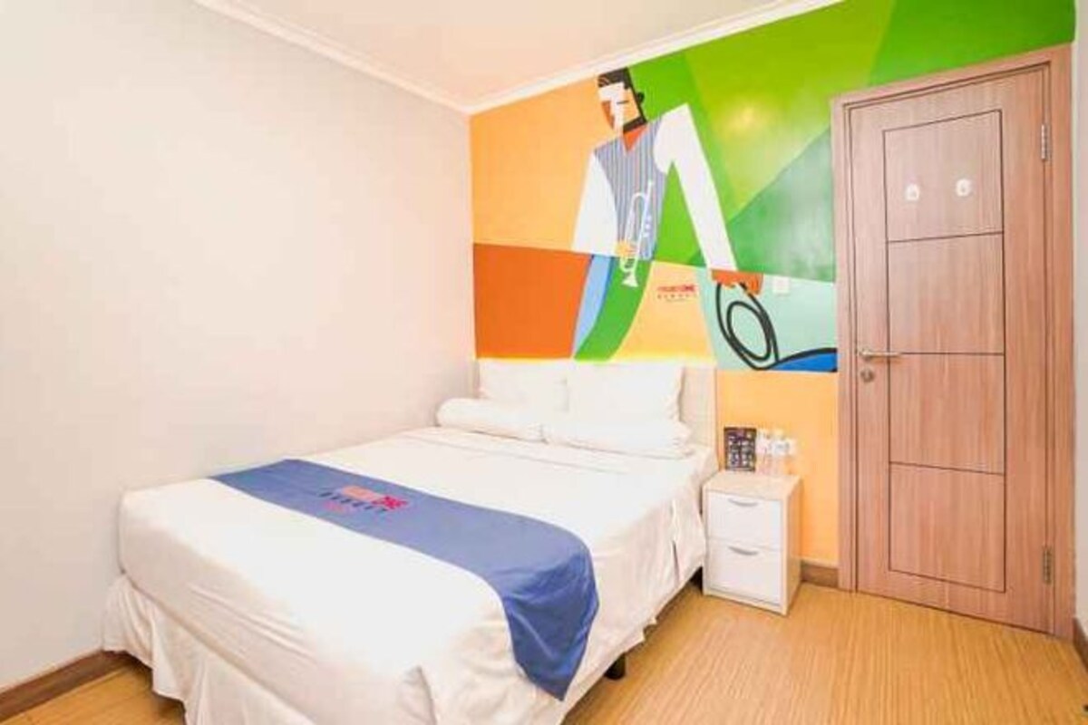 Habitación de hotel con una cama, una mesita de noche, una obra de arte en la pared y una puerta de madera.