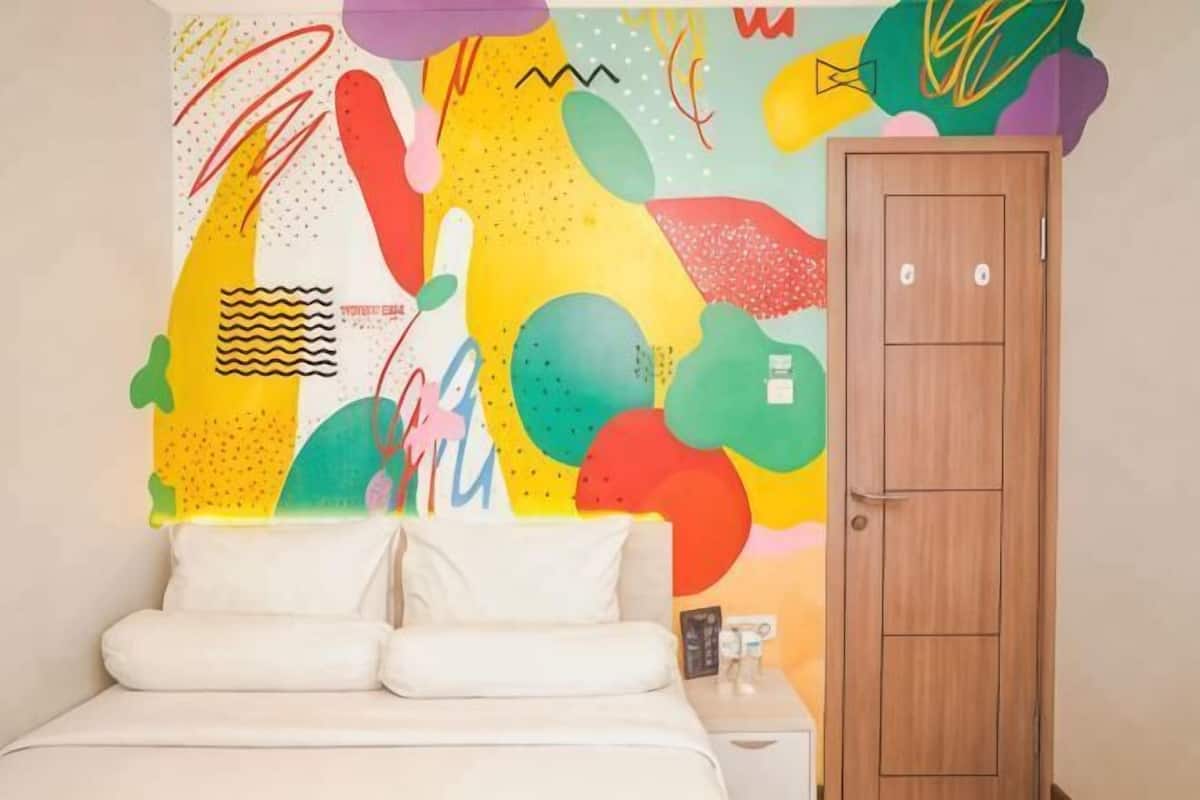 A bedroom with a colorful abstract wall art, a wooden door, and a white bed.
