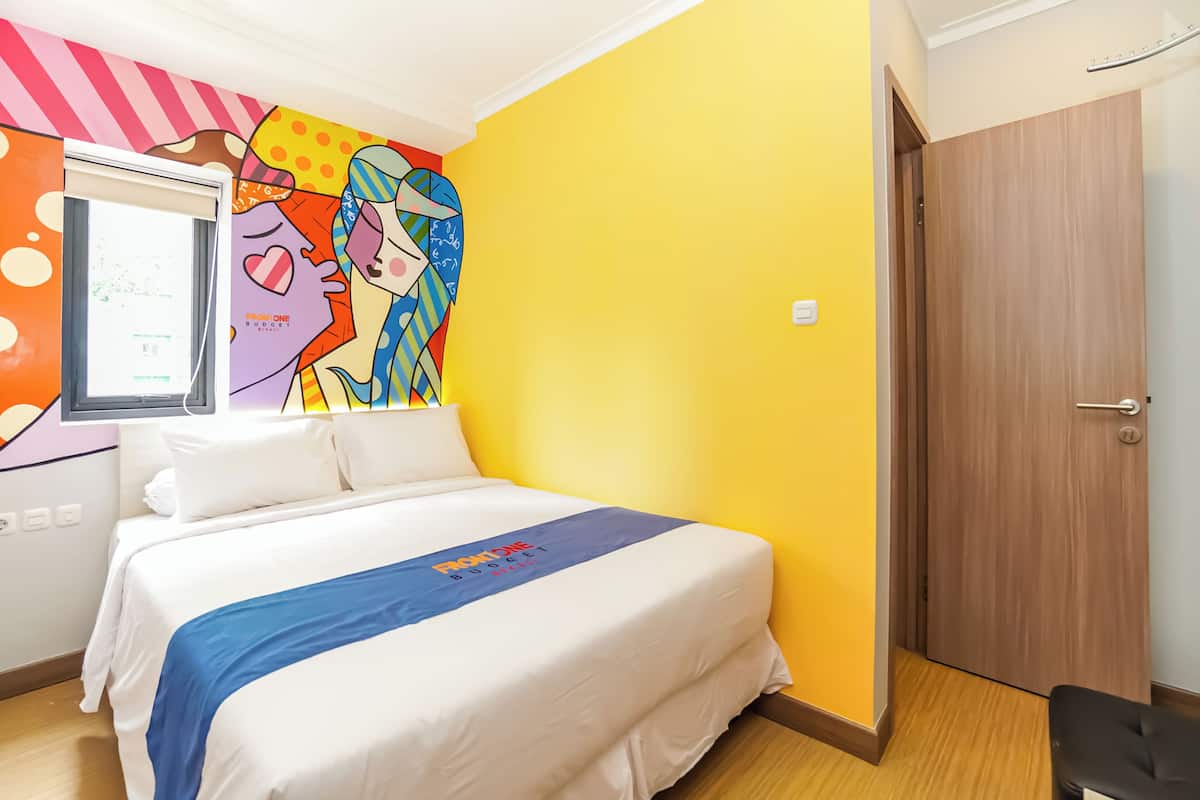 A hotel room with a bed, a colorful mural, a wooden door, and a window.