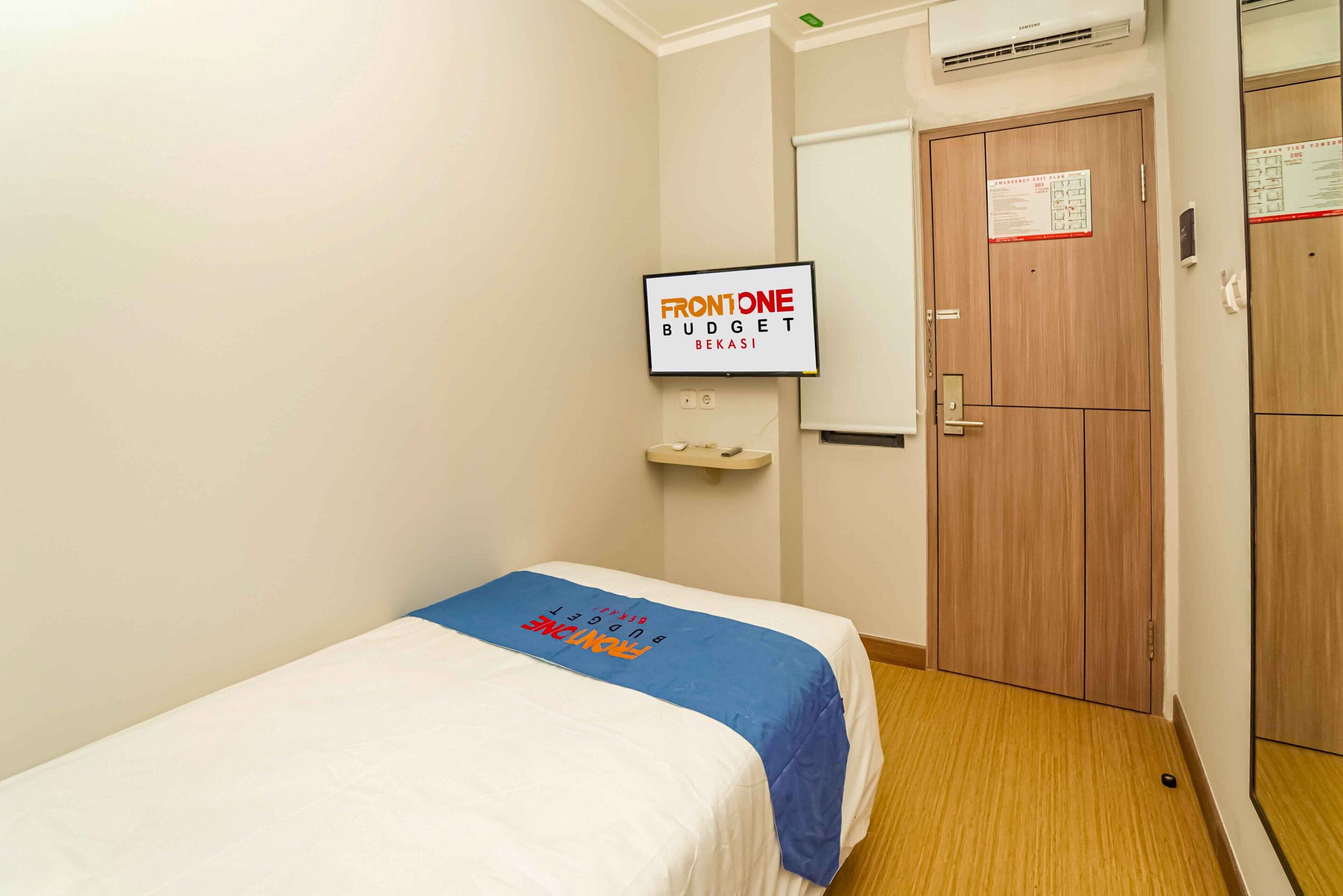 A hotel room with a bed, a sign on the wall, a wooden door, and a small shelf.