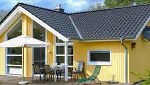 Et gult hus med stor terrasse, overdækket patio og parabolantenne.