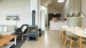 Et moderne køkken med en central ø, et spiseområde med træstole, en sofa og en brændeovn.
