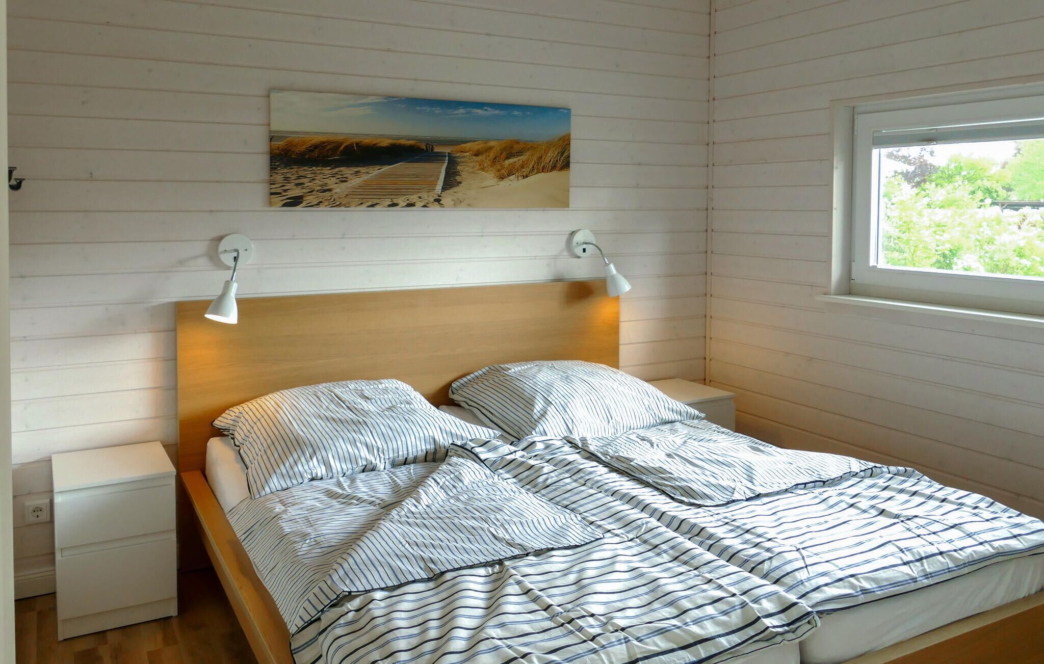 A bedroom with a wooden headboard, a single bed with striped bedding, a nightstand, a bedside lamp, and a painting of a beach scene.