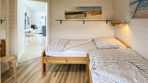 Et soveværelse med en træseng, stribet sengetøj, et maleri af en strand og et skrivebord, der kan ses gennem en åben dør.