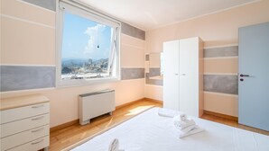 A modern bedroom with a large window, a bed with white linens, a wardrobe, and a radiator. - Nice apartment in Genova with WiFi (Genova)
