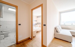 A modern apartment with a bathroom, a bedroom with a bed and nightstand, and a living area with a sofa and a window.