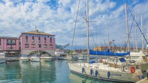 A marina with several boats docked, a building with a pink facade, and a clear blue sky. - Nice apartment in Genova with WiFi (Genova)