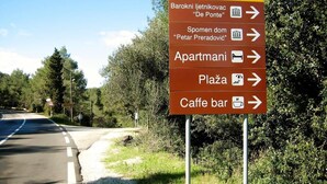 Un panneau de signalisation indiquant différentes directions grâce à de nombreuses flèches pointant vers divers lieux, notamment un bar, des appartements, une place et un café.