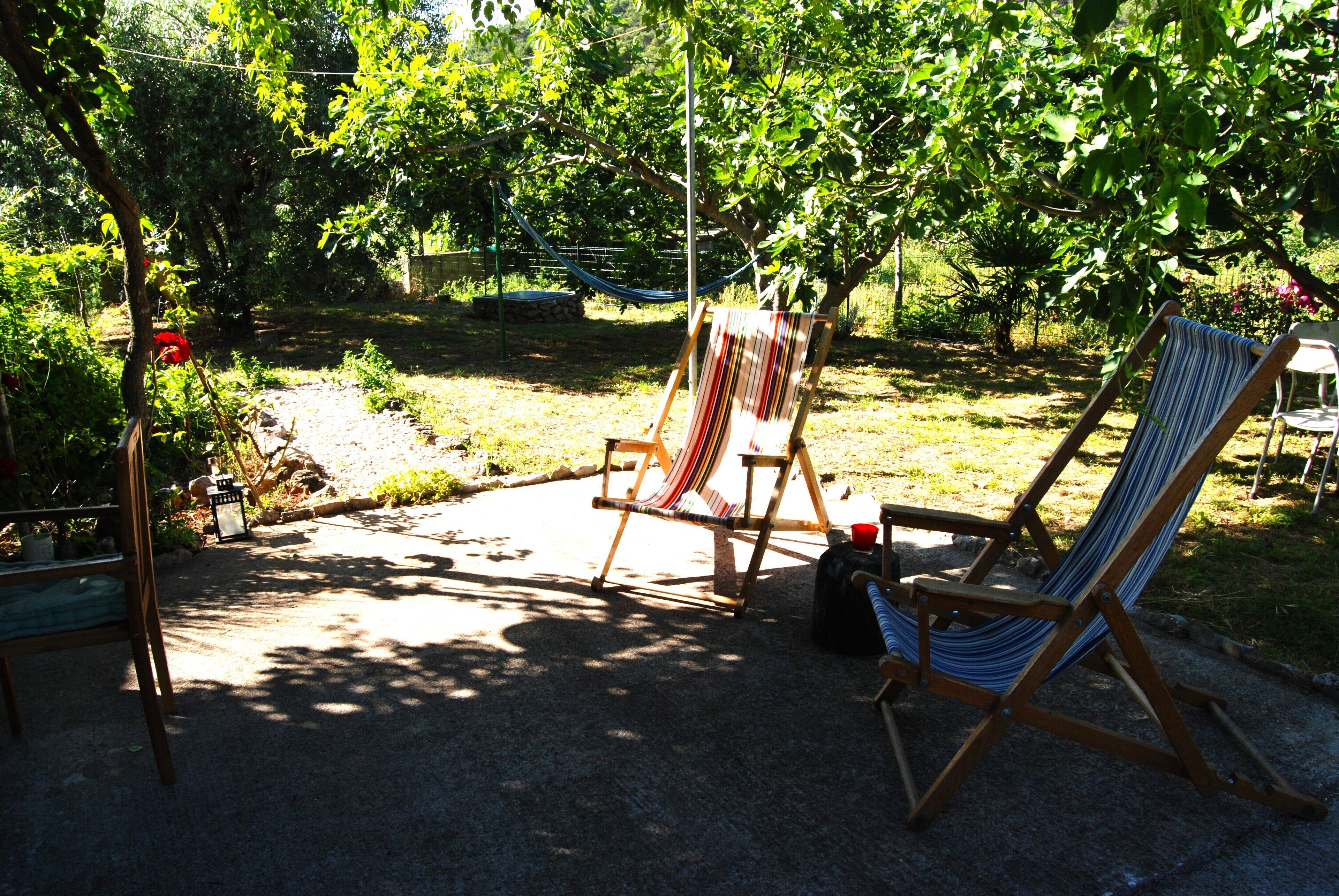 Un fauteuil suspendu, un fauteuil à rayures et un fauteuil en bois, le tout installé dans un jardin.