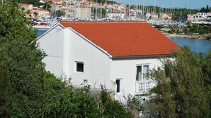 Un bâtiment blanc coiffé d’un toit rouge, entouré de verdure et donnant sur une marina où sont amarrés de nombreux bateaux.
