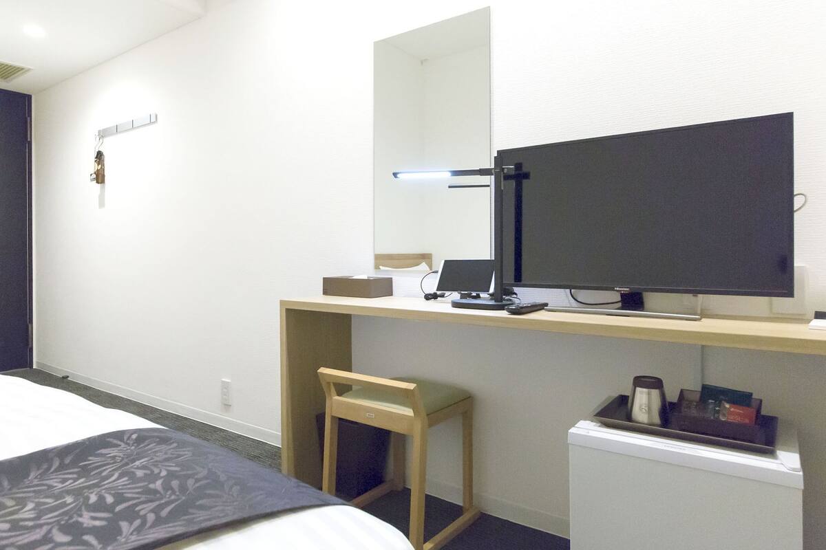 Habitación de hotel con cama, escritorio con computadora, silla, refrigerador pequeño y espejo.
