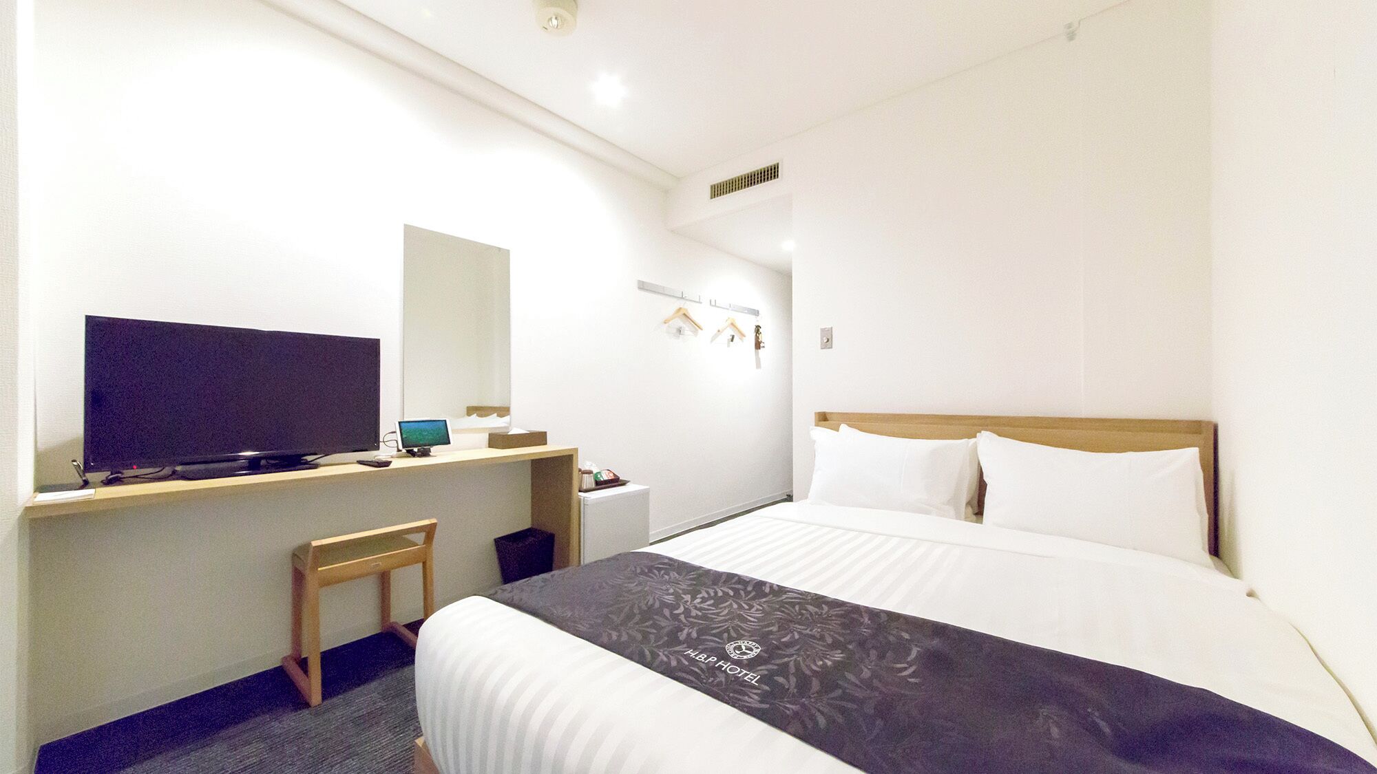 Una habitación de hotel con una cama, un escritorio con una computadora, un televisor y una silla pequeña.