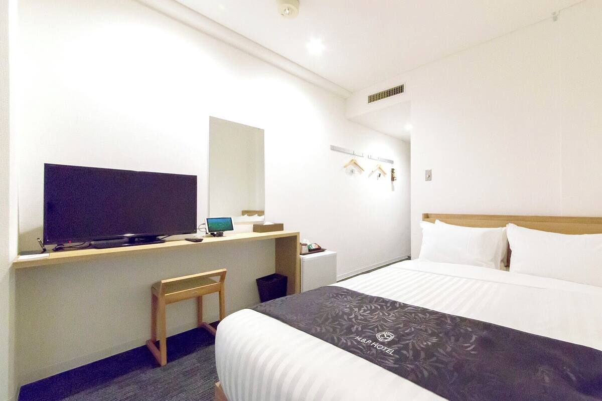 Una habitación de hotel con una cama, un escritorio con una computadora, un televisor y una silla pequeña.
