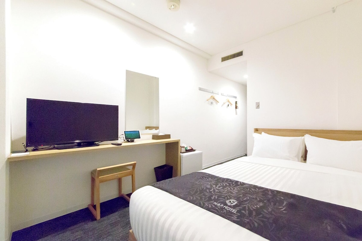 Une chambre d’hôtel avec un lit, un bureau avec un ordinateur, une télévision et une petite chaise.