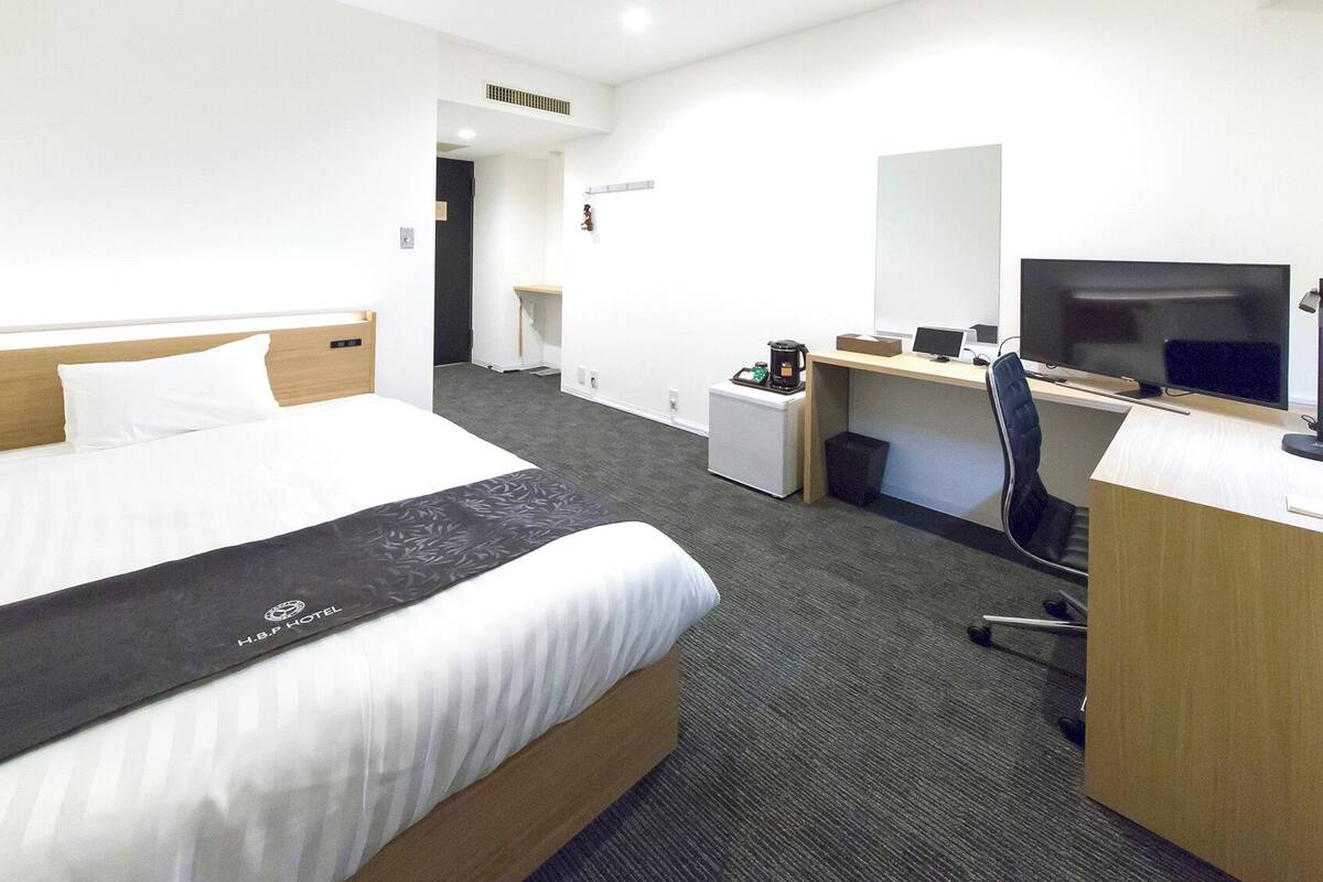 Una habitación de hotel con cama, escritorio, silla, televisor y cafetera.