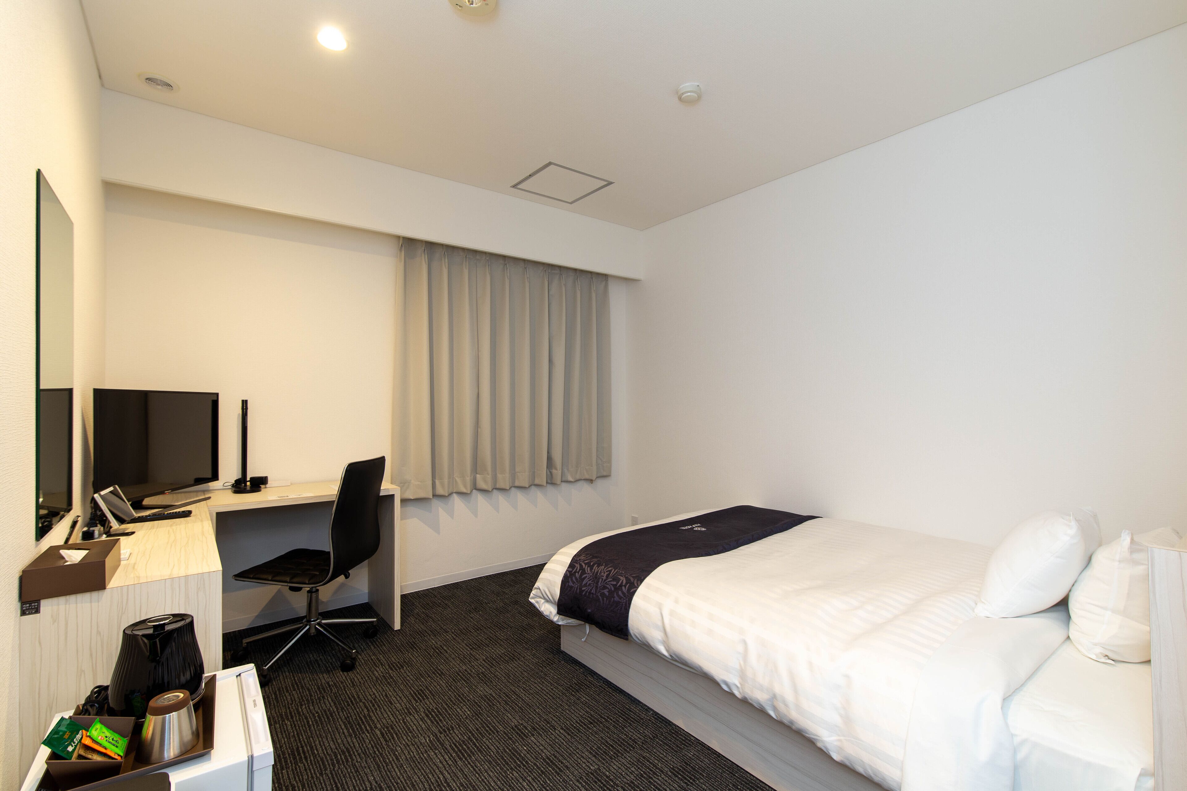 Une chambre d’hôtel avec un lit, un bureau avec un ordinateur, une chaise et une fenêtre avec des rideaux.