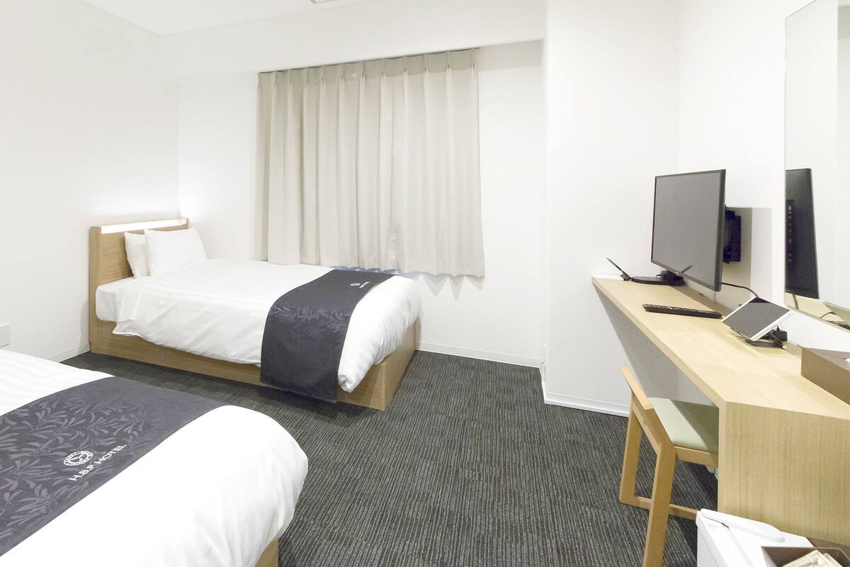 Habitación de hotel con dos camas, un escritorio con computadora, televisor y ventana con cortinas.