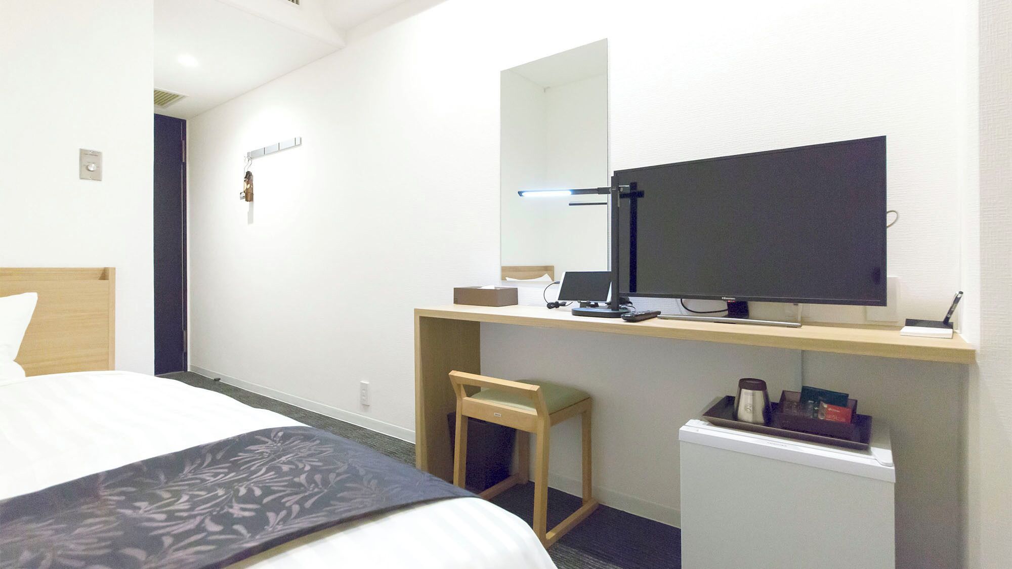Habitación de hotel con una cama, un escritorio con computadora, una silla, un refrigerador pequeño y un espejo.