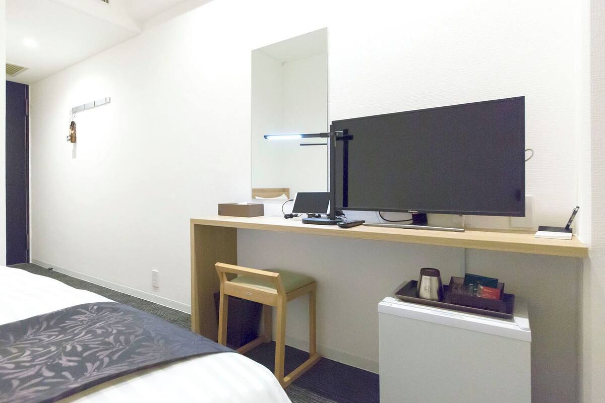 Habitación de hotel con una cama, un escritorio con computadora, una silla, un refrigerador pequeño y un espejo.
