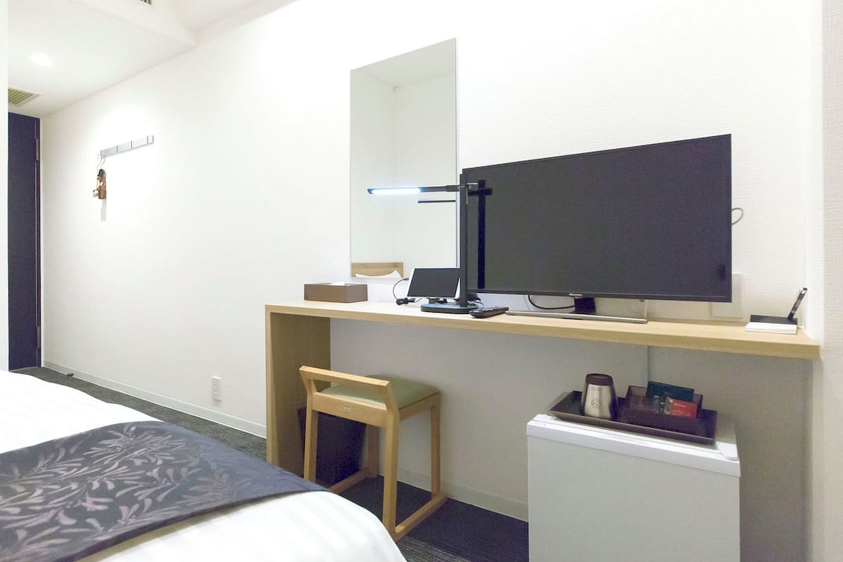 Une chambre d’hôtel équipée d’un lit, d’un bureau avec un ordinateur, d’une chaise, d’un petit réfrigérateur et d’un miroir.
