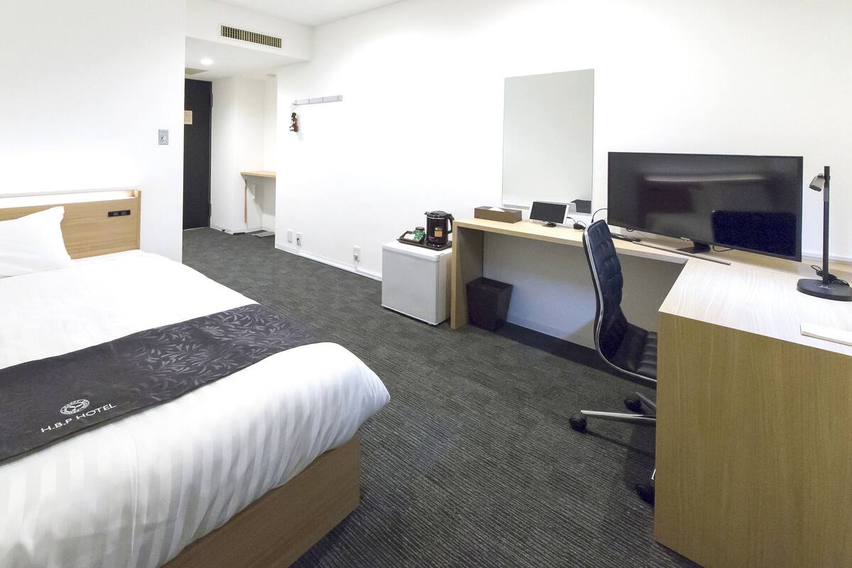Habitación de hotel con cama, escritorio, computadora, televisor y cafetera.