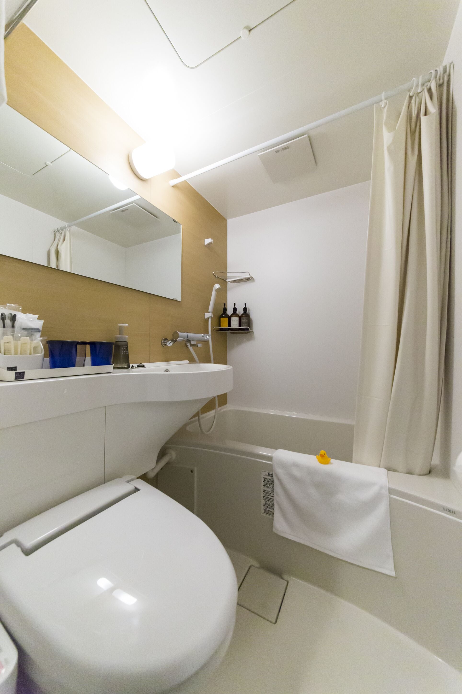 Ein modernes Badezimmer mit Toilette, Waschbecken mit Spiegel darüber, Dusche mit Vorhang und Handtuchhalter.