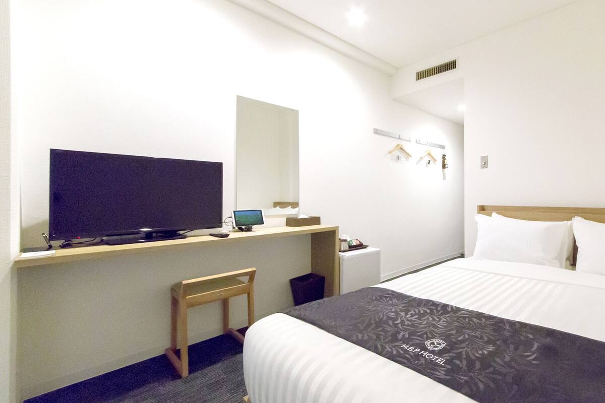 Una habitación de hotel con cama, escritorio, computadora, televisor y una mesita.