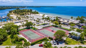 An aerial view of a coastal area with a marina, tennis courts, and a beach.