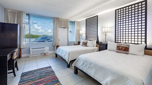 A hotel room with two beds, a desk, a chair, a TV, and a window with a view of a car and greenery.