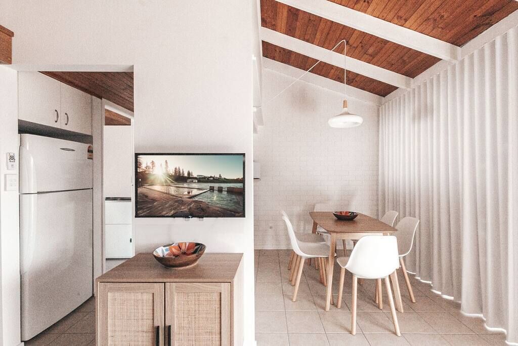 A modern kitchen with white cabinets, a wooden dining table, and a large window with curtains.