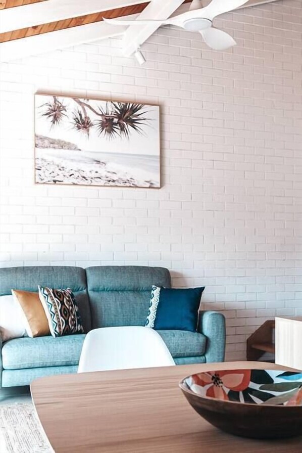 A living room with a blue sofa, a white coffee table, and a framed picture on the wall. - BAY PROPERTIES | Pippi Beach Studio (Yamba)