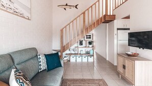 A modern living room with a grey sofa, wooden staircase, and a flat-screen TV. - BAY PROPERTIES | Pippi Beach Studio (Yamba)
