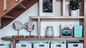 A wooden shelf with decorative fish, a framed picture, a book titled 'FAMILY', and woven baskets. - BAY PROPERTIES | Pippi Beach Studio (Yamba)