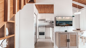 A modern kitchen with white cabinets, a wooden ceiling, and a large window overlooking the ocean. - BAY PROPERTIES | Pippi Beach Studio (Yamba)