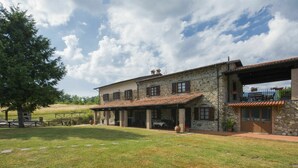 Une maison en pierre avec un toit en tuiles, un patio couvert et une cour gazonnée.