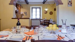 Un coin repas avec une table dressée pour quatre personnes, une bouteille de vin et un panier de fruits.