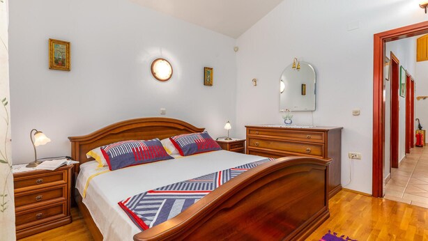 A bedroom with a wooden bed, bedside tables, a nightstand, a dresser, a mirror, and a door. - Beautiful home in Muntic (Muntic)