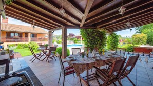 Une terrasse extérieure avec une table dressée pour le repas, entourée de chaises, et située sous une pergola en bois.