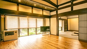 Una habitación amplia con suelo de madera, grandes puertas correderas de vidrio, un televisor de pantalla plana y una puerta corredera tradicional con listones verticales.
